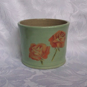May include: A light green ceramic planter with two orange roses painted on the side.