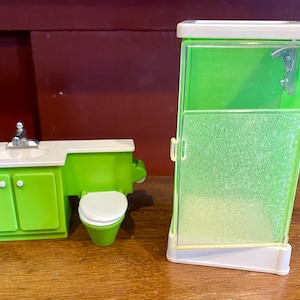 May include: A miniature lime green bathroom set, including a vanity with a sink, a toilet, and a shower stall. The set has white accents and is made of plastic. The shower has a textured door and a silver shower head.