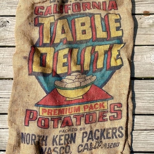 May include: A vintage burlap potato sack with bold text reading "US No. 1 California Table Delite Potatoes." The sack features a colorful graphic of potatoes and is from North Kern Packers, Vasco, CA.