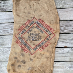 May include: A vintage burlap sack with red and blue printed text. The text reads "REG.U.S.PAT.OFF. GRADED POTATOES SOUTH SHORE TRADE MARK LONG ISLAND BRAND PACKED BY J.C. MAGEE 100 LBS NET BRIDGEHAMPTON N.Y. WATER MILL N.Y. U.S. No. 1".