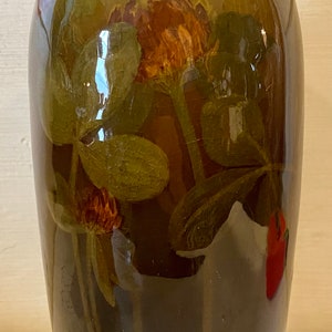 May include: A brown ceramic vase with a floral design featuring green leaves and red and orange flowers. The vase has a glossy finish.
