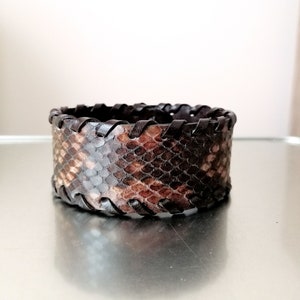 Peut inclure: Un bracelet en cuir marron avec un motif peau de serpent et un bord cousu.