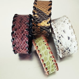 Peut inclure: Cinq bracelets en cuir avec différents motifs et couleurs. Les bracelets sont en cuir marron, beige, blanc, vert et rouge. Chaque bracelet est orné d'une couture noire sur les bords.