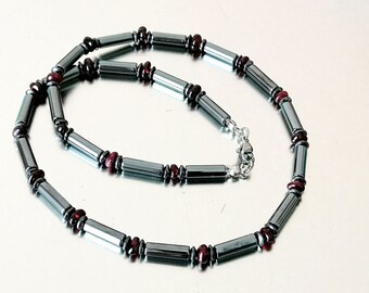 May include: A silver necklace with black and red beads. The necklace is made of hematite and garnet beads.