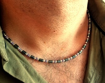 May include: A close-up of a man's chest with a silver and purple beaded necklace. The necklace is made of small, round beads and is worn around the neck.