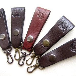 May include: Five leather keychains with different animal designs. The keychains are brown and red with metal rings and snaps. The animal designs include a wolf, a bear, a deer, a bird, and a lion.