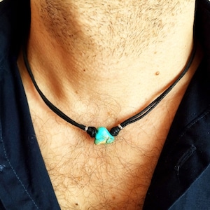 以下が含まれることがあります： 黒い革ひもネックレスにターコイズのペンダントがついたネックレス
