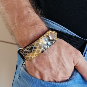 May include: A gold and black leather bracelet with a silver snap closure. The bracelet has a geometric pattern.