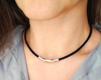 May include: A black leather choker necklace with a silver bar pendant.