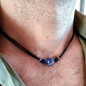 Puede incluir: Un collar sencillo de cordón de cuero negro con una sola cuenta redonda de piedra preciosa púrpura.