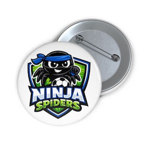 May include: A round pin-back button featuring a graphic of a black spider wearing a blue headband, holding a soccer ball. The design includes a shield-shaped background with green and blue accents and the text NINJA SPIDERS in bold letters.