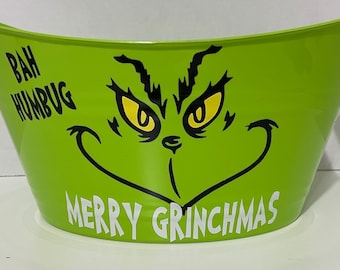May include: Green plastic Grinch-themed Christmas bucket with a black and white Grinch face and the text "Bah Humbug" and "Merry Grinchmas".