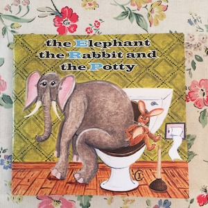 May include: A children's book cover titled "the Elephant the Rabbit and the Potty." The illustration shows an elephant and a rabbit on a toilet. The background features patterned wallpaper and a wooden floor.