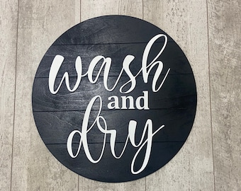 Puede incluir: Un letrero redondo de madera con fondo negro y letras blancas que dice "wash and dry".
