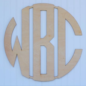May include: A wooden monogram with the letters "W R C" cut out in a circle. The monogram is made of light brown wood and has a natural finish.