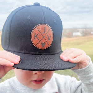 May include: A black baseball cap with a brown leather patch featuring the letters "KJV" in a circle with a cross.