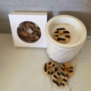 May include: White ceramic wax warmer with a textured design. The warmer has a round opening at the top and a small white box with a window showing wax melts in the shape of donuts with a brown and white striped design.