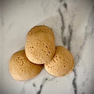 Puede incluir: Tres galletas redondas y ligeramente hinchadas de color marr&oacute;n claro sobre una superficie de m&aacute;rmol blanco.
