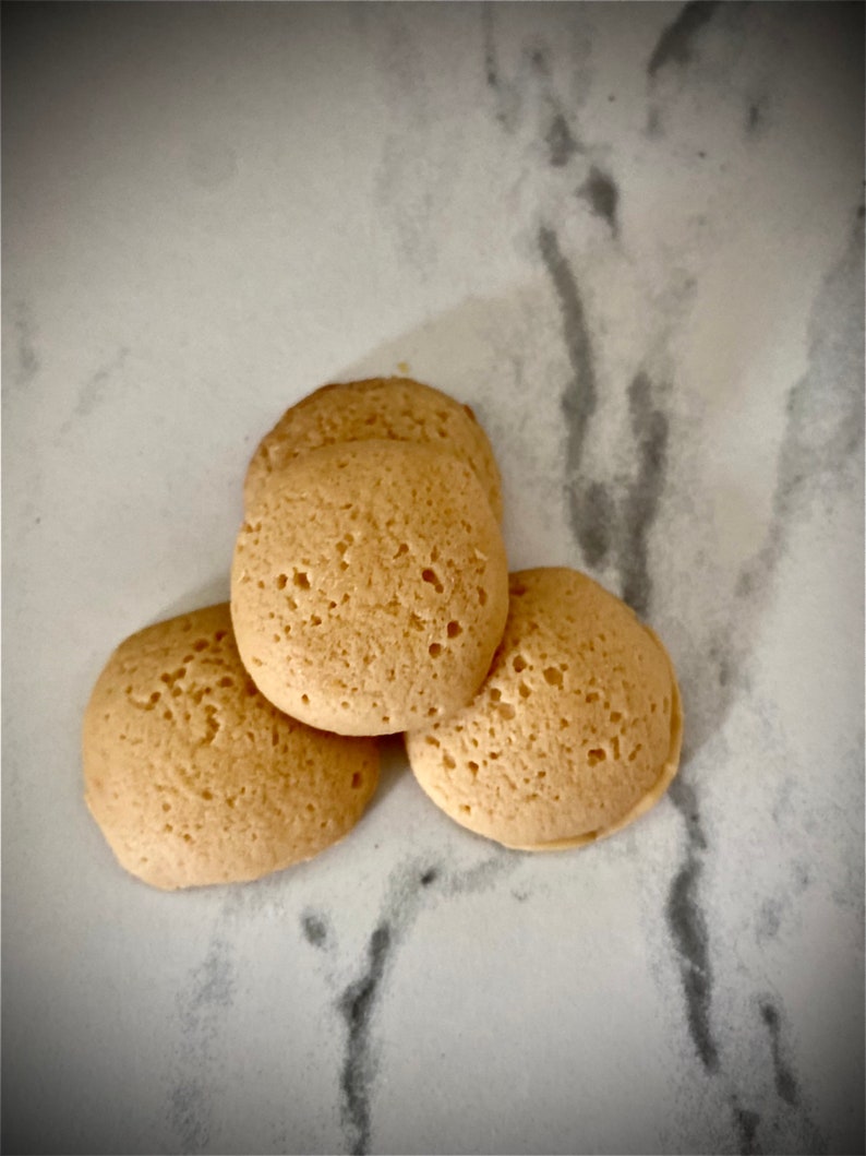 Puede incluir: Tres galletas redondas y ligeramente hinchadas de color marr&oacute;n claro sobre una superficie de m&aacute;rmol blanco.