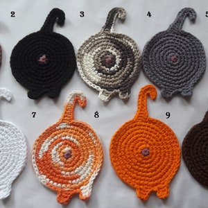 May include: Nine crocheted cat's bottom coasters in various colours, including brown, black, grey, white, orange, and a swirl pattern. Each coaster has a pink button sewn in the centre and a crocheted tail.