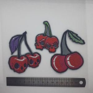 May include: Three embroidered iron-on patches of red cherries with skull faces. The cherries are on grey stems with green leaves.