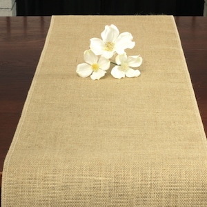 May include: A natural burlap table runner with a woven texture. White flowers are arranged in the center of the runner.