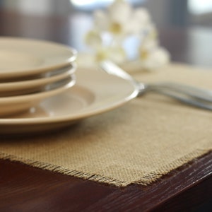 May include: A set of four white ceramic plates stacked on top of each other on a brown burlap placemat. The plates are on a dark brown wooden table.