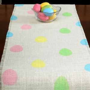May include: A white burlap table runner with colorful polka dots in pink, yellow, blue, and green. The runner is perfect for a spring or Easter table setting.