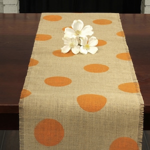 May include: A burlap table runner with orange polka dots. The runner is frayed on the edges and has a rustic look.