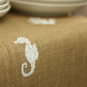 May include: A brown burlap table runner with a white seahorse and starfish design.