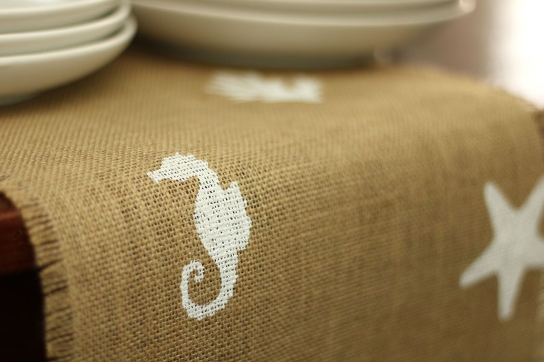 May include: A brown burlap table runner with a white seahorse and starfish design.