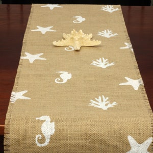 May include: A beige burlap table runner with a white seahorse, starfish, and coral design.
