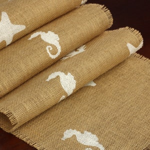 May include: A brown burlap table runner with a frayed edge features a white starfish and seahorse design.