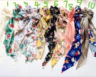 Puede incluir: Una colección de diez coleteros con cintas de tela adjuntas. Los coleteros presentan varios patrones florales, de lunares y temáticos de vacaciones en colores como rojo, azul, amarillo y rosa. Las cintas añaden un elemento decorativo.