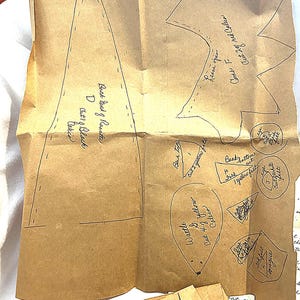 May include: A brown paper pattern with handwritten instructions and cut-out shapes for a craft project. The pattern includes shapes for a beak, wattle, and other parts, with text like "Cut 2 of yellow felt".
