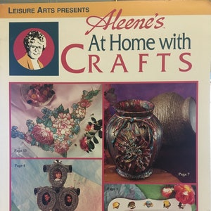 Puede incluir: Una portada de revista titulada "Aleene's At Home with Crafts" de Leisure Arts. La portada presenta proyectos de manualidades, incluyendo un arreglo floral, un jarrón decorativo, un marco de fotos múltiple y una bandeja decorativa con un diseño floral y de tazas de té. También incluye el texto "20 Terrific Projects."