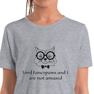 Puede incluir: Camiseta gris para jóvenes con una ilustración en blanco y negro de un gato con gafas y pajarita. El texto "Lord Fancypaws and I are not amused" está impreso debajo del gato.