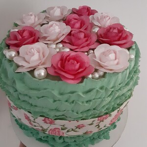 May include: A green cake with white and pink frosting and a floral design. The cake is decorated with pink and white roses and pearl-like sprinkles.