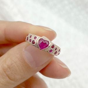 May include: A gold ring featuring a heart-shaped ruby gemstone surrounded by smaller ruby gemstones.