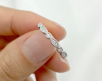 May include: A delicate silver ring with a repeating pattern of marquise-shaped settings, each set with small, sparkling gemstones. The ring is held against a soft, white background, highlighting its intricate design and elegant simplicity.