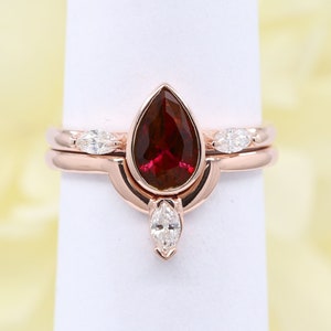 May include: A pear-shaped ruby gemstone ring set in a rose gold band with a matching rose gold band featuring pear-shaped diamonds.