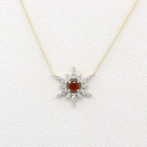 May include: A gold necklace with a red gemstone surrounded by smaller white gemstones in a starburst design.