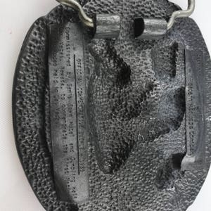 May include: A textured, oval-shaped metal belt buckle. The buckle has a detailed design and includes text that reads "OFFICIAL COMMEMORATIVE BUCKLE 1985" and "Las Vegas, Nevada". The buckle is a commemorative item.