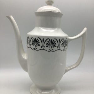 Può includere: Caffettiera in ceramica bianca con un design geometrico in bianco e nero. La caffettiera ha un coperchio con un pomo in cima.
