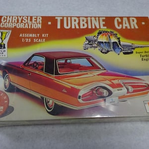 May include: A vintage Chrysler Turbine Car assembly kit, 1/25 scale, featuring a red and brown car illustration. The box includes text: "CHRYSLER CORPORATION - TURBINE CAR - ASSEMBLY KIT". The box also has a gold cup series logo.