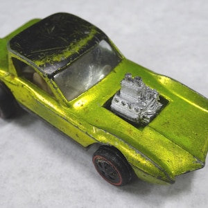 May include: Lime green toy car with a black roof and silver engine detail. The vintage die-cast model has black wheels with red rims. The car's paint shows signs of wear, suggesting it is a collectible item.