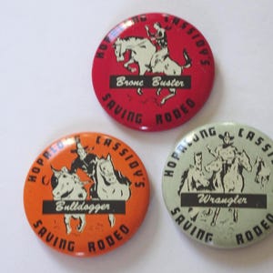 May include: Three vintage Hopalong Cassidy Saving Rodeo pinback buttons. The buttons are red, orange, and light green with illustrations of cowboys and horses. Text includes "Bronc Buster", "Bulldogger", and "Wrangler".