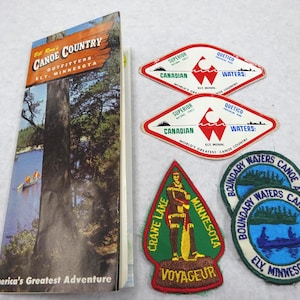 May include: A collection of vintage camping and canoeing ephemera. Includes a brochure titled "Canoe Country Outfitters Ely, Minnesota" and several embroidered patches with canoe and lake themes. Patches feature text like "Boundary Waters Canoe Area" and "Voyageur".