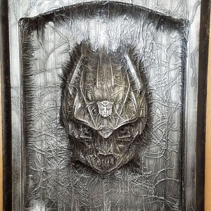 May include: A black framed wall decor with a silver 3D sculpted image of a robot head. The robot head has a cracked and weathered texture.