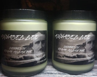 Può includere: Due barattoli di vetro colorato di verde con coperchi neri. Ogni barattolo ha un'etichetta con il testo "ANNABEL LEE" e "INSPIRED BY EDGAR ALLAN POE", insieme a un ritratto di un uomo. I barattoli sono esposti su una superficie di legno.